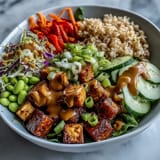 Crispy golden tofu cubes nestled on brown rice with colorful veggies and drizzled creamy peanut sauce in a Peanut Tofu Power Bowl.