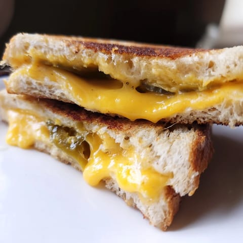 A close-up of golden, buttery Cheddar Jalapeño Grilled Cheese, oozing melted cheese and tangy pickled jalapeños.