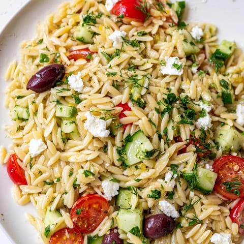 Colorful Greek Orzo Salad served in a white bowl, featuring red onion, olives, and fresh herbs.