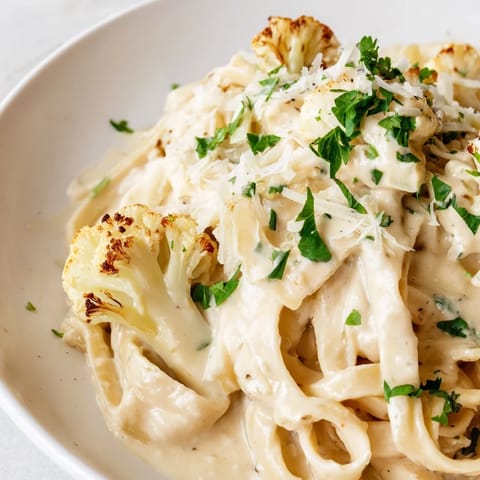 Creamy roasted cauliflower alfredo sauce coats fettuccine, garnished with fresh parsley and a sprinkle of Parmesan cheese.