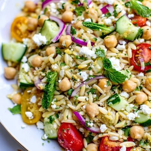 Vibrant bowl of chilled Lemony Chickpea Orzo Salad featuring chickpeas, mint, and lemon zest, served as a light lunch.
