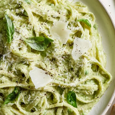 Steaming green pea Alfredo pasta in a skillet, featuring a vibrant sauce and freshly grated Parmesan.  
