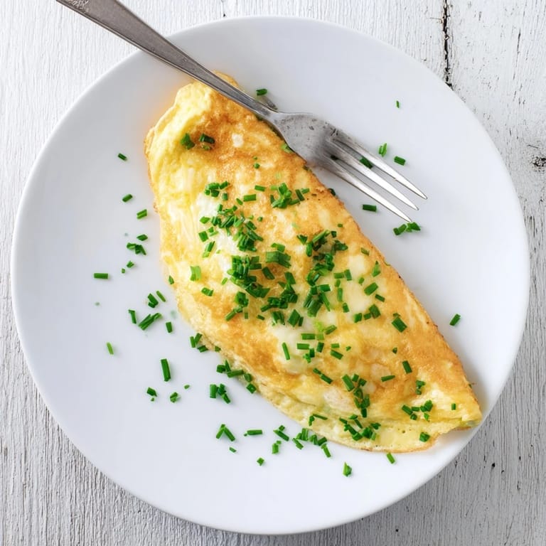 Perfectly folded cheesy omelet garnished with fresh chives, paired with buttered toast and coffee nearby.