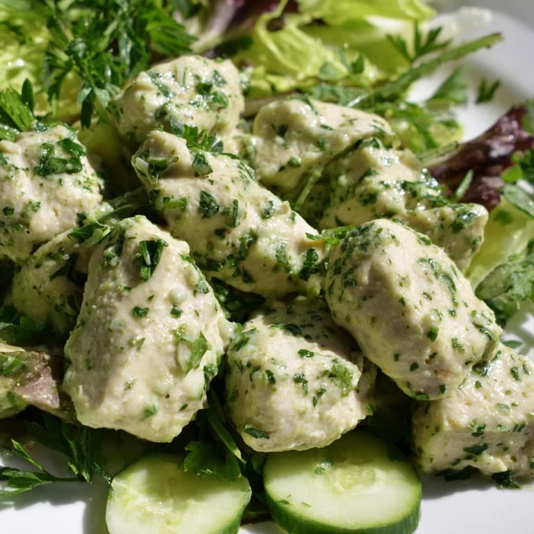 Vibrant bowl of Green Goddess Chicken Salad with golden chicken pieces, fresh herbs, and sliced avocado on colorful greens, ready to enjoy.