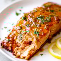 Glossy honey garlic glazed salmon fillets, caramelized and tender, served alongside lemon wedges and fresh parsley.