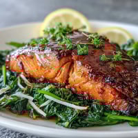 Four miso-glazed salmon fillets bake to a glossy, caramelized finish, resting on a vibrant bed of sautéed spinach for a quick, healthy dinner.  