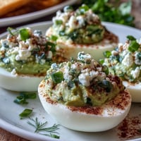 Green avocado deviled eggs with creamy filling and fresh herbs on a white platter, perfect for spring parties and healthy appetizers.